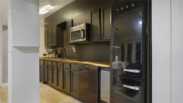 kitchen featuring a sink, light wood-style floors, stainless steel microwave, dishwashing machine, and freestanding refrigerator