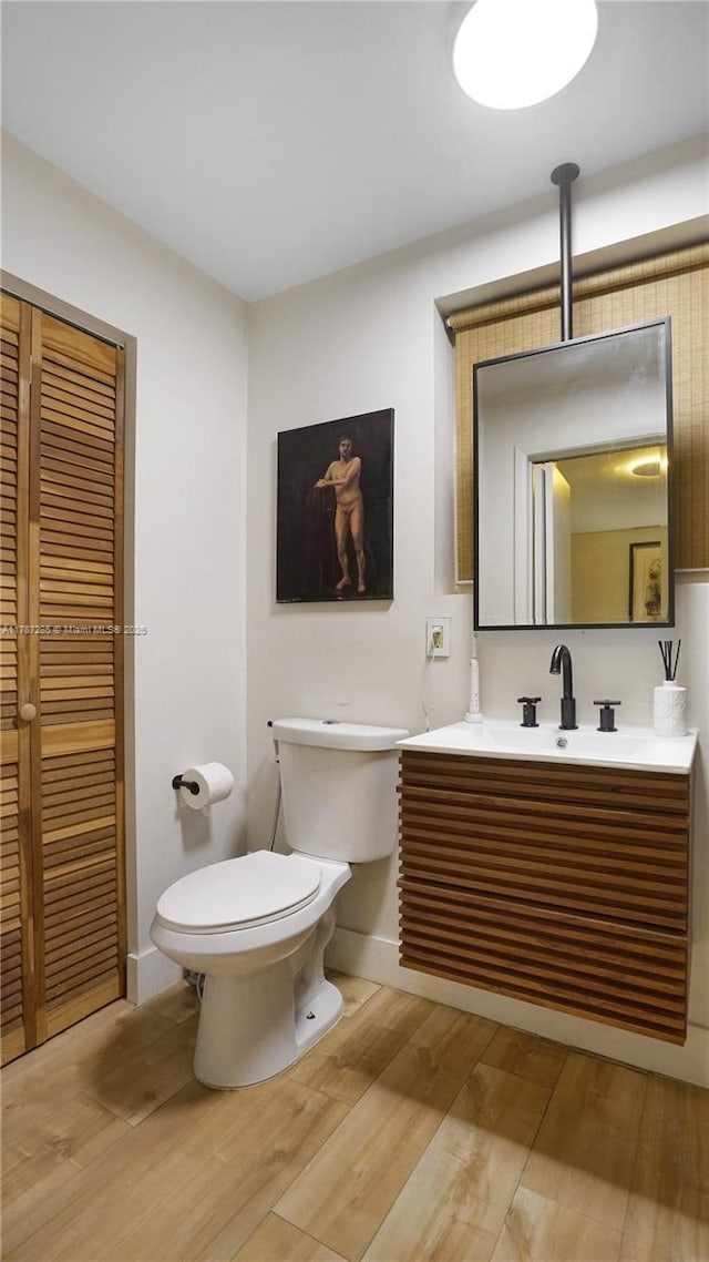 bathroom with toilet, vanity, wood finished floors, and baseboards