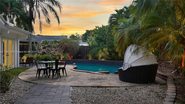 pool at dusk featuring an outdoor pool, a fenced backyard, and a patio