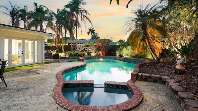 pool at dusk with a fenced backyard, french doors, a pool with connected hot tub, and a patio