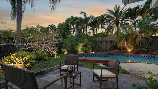 patio terrace at dusk featuring a fenced backyard and a fenced in pool
