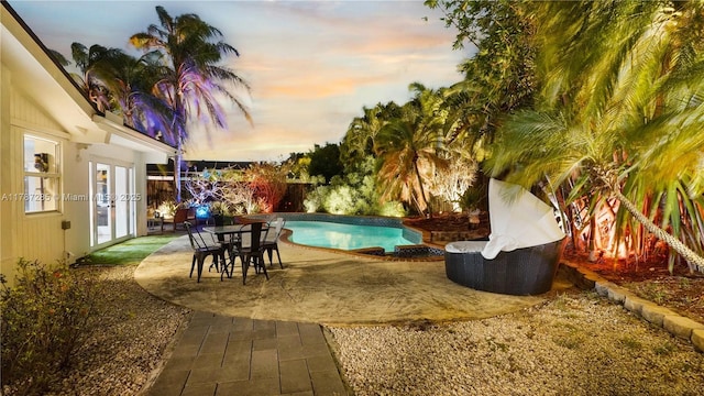 pool at dusk with a fenced backyard, a patio area, a fenced in pool, and french doors
