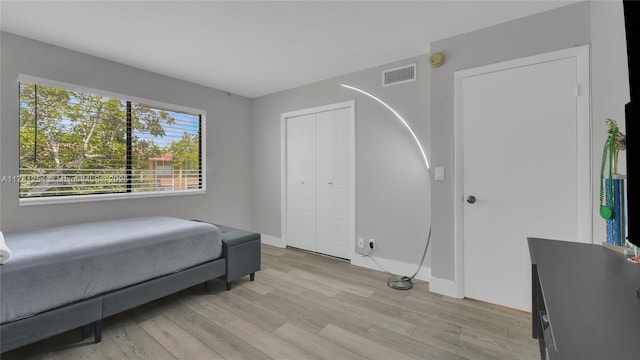 bedroom with light wood-type flooring, baseboards, visible vents, and a closet