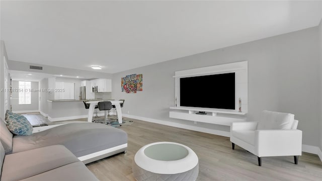 living area with baseboards, light wood-style floors, and visible vents