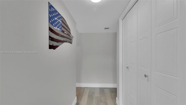 hallway with wood finished floors, visible vents, and baseboards