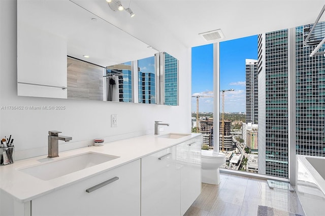 full bath featuring a tub to relax in, a wall of windows, double vanity, and toilet