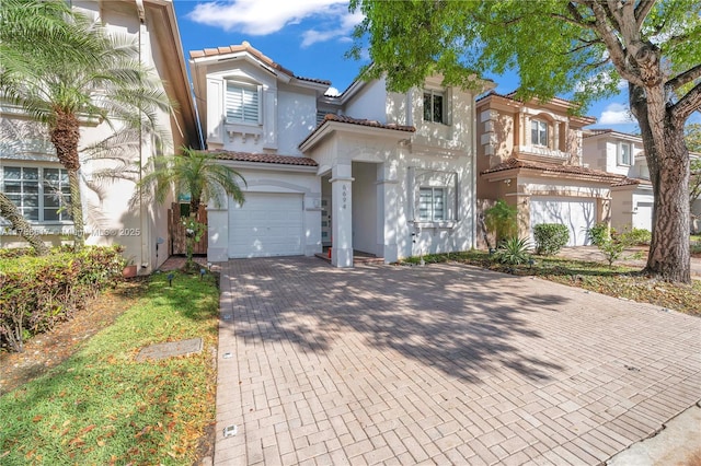 mediterranean / spanish-style house featuring a tile roof, an attached garage, stucco siding, and decorative driveway