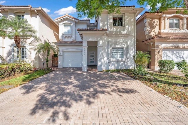 mediterranean / spanish house with a garage, a tile roof, stucco siding, and decorative driveway