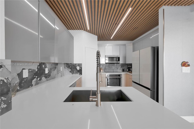 kitchen featuring stainless steel appliances, light countertops, a sink, modern cabinets, and decorative backsplash