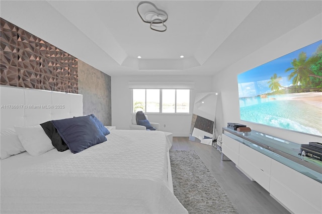 bedroom with wood finished floors, a tray ceiling, and recessed lighting