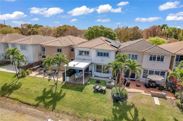 rear view of property with roof mounted solar panels, fence, stucco siding, a patio, and a lawn