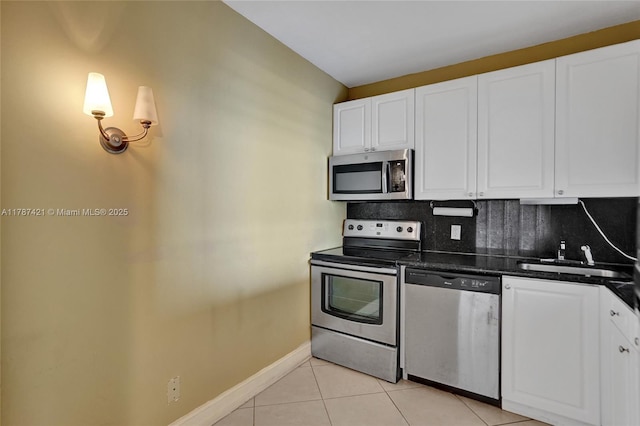 kitchen with dark countertops, tasteful backsplash, a sink, light tile patterned flooring, and appliances with stainless steel finishes