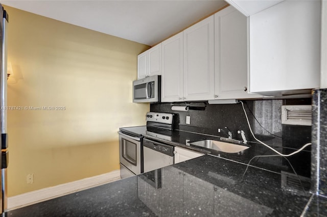 kitchen with stainless steel appliances, a sink, baseboards, white cabinetry, and decorative backsplash