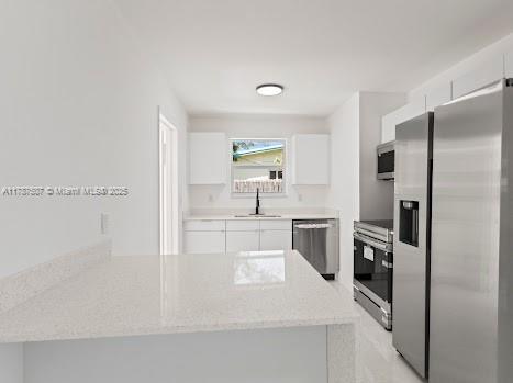 1310 NW 41st St, Oakland Park, FL 33309 - kitchen with a sink, light stone counters, white cabinets, a peninsula, and stainless steel appliances