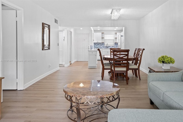 living area featuring a textured ceiling, light wood-type flooring, visible vents, and baseboards