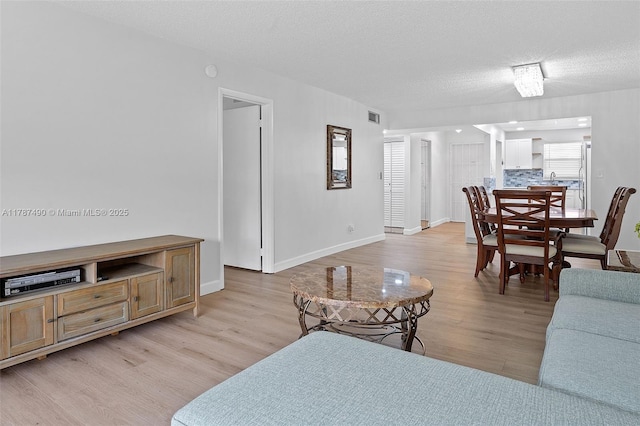 living room featuring light wood-style floors, baseboards, visible vents, and a textured ceiling
