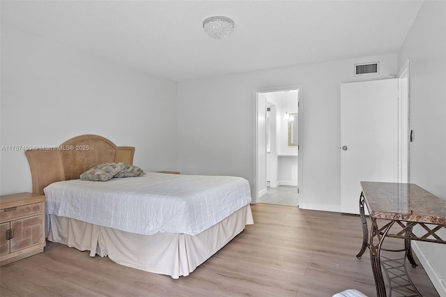 bedroom featuring baseboards, wood finished floors, visible vents, and ensuite bathroom