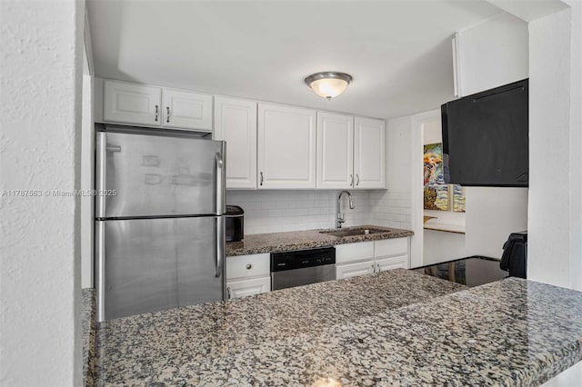 kitchen with a sink, dark stone countertops, white cabinetry, decorative backsplash, and appliances with stainless steel finishes
