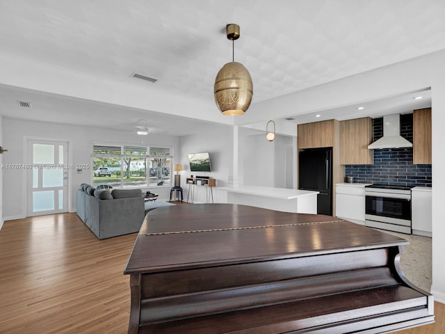 kitchen with white electric range oven, modern cabinets, wall chimney exhaust hood, visible vents, and freestanding refrigerator