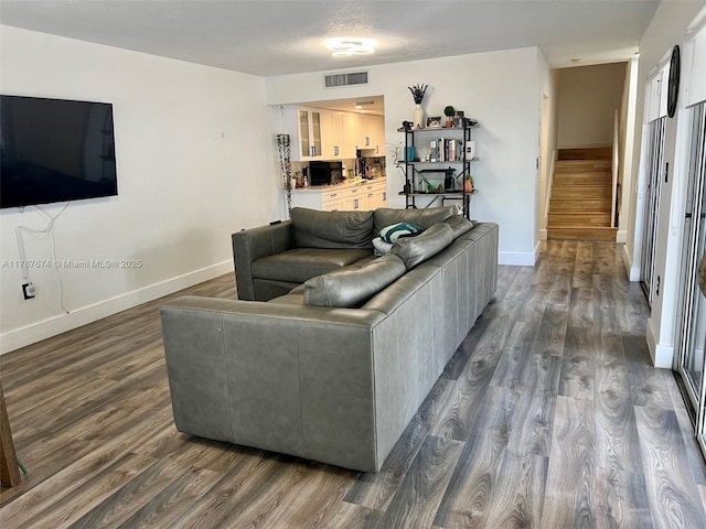 living area featuring dark wood-type flooring, stairway, visible vents, and baseboards