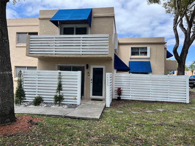 back of house featuring fence, a balcony, and stucco siding