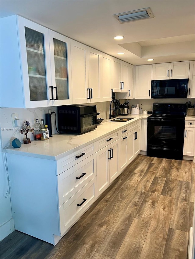 kitchen with white cabinets, dark wood-style floors, a sink, and black appliances