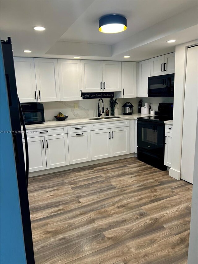 kitchen featuring a raised ceiling, a sink, recessed lighting, and black appliances