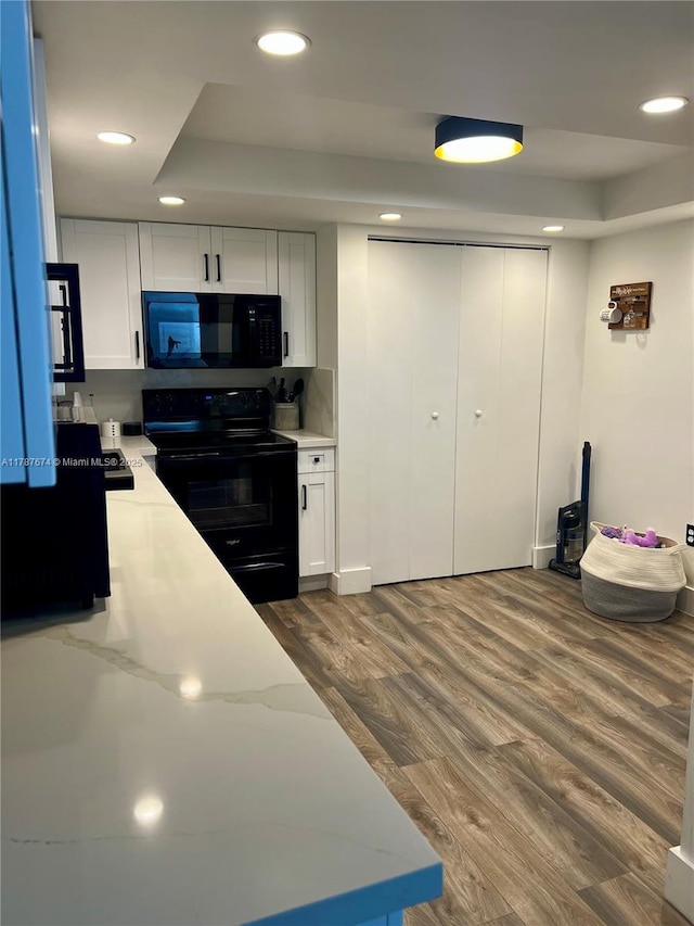 kitchen with a tray ceiling, recessed lighting, black appliances, and dark wood finished floors