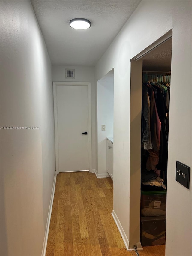 hallway featuring baseboards, visible vents, and light wood-style flooring