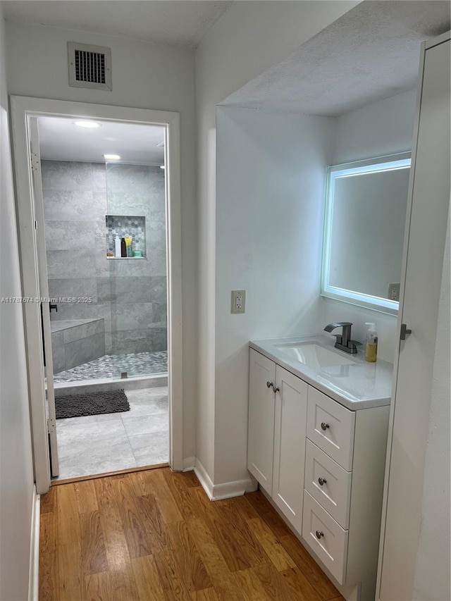 full bathroom featuring wood finished floors, vanity, visible vents, baseboards, and a walk in shower