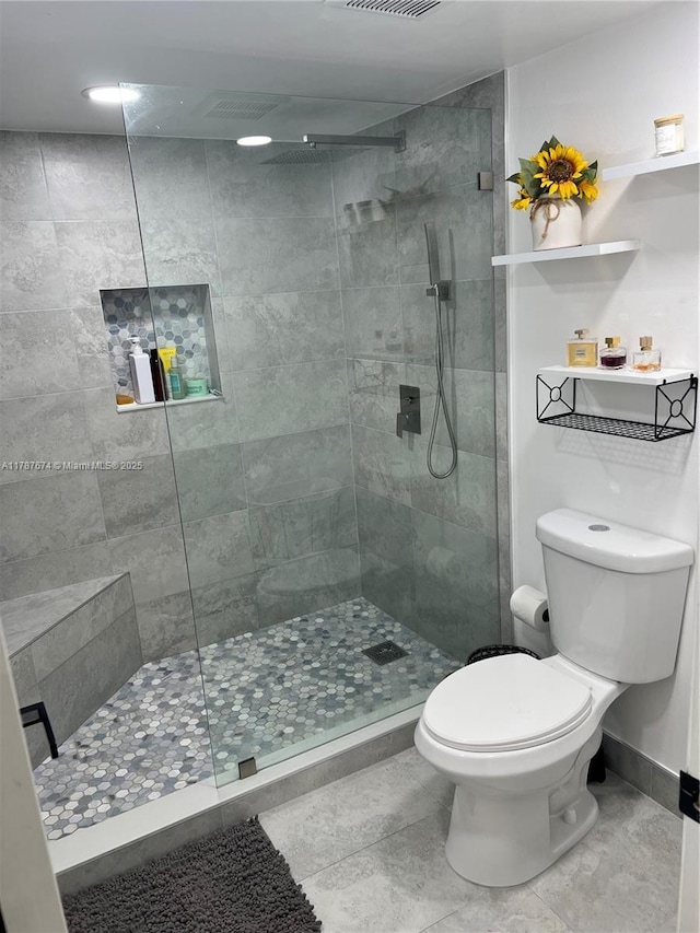 full bathroom with visible vents, tiled shower, baseboards, and toilet
