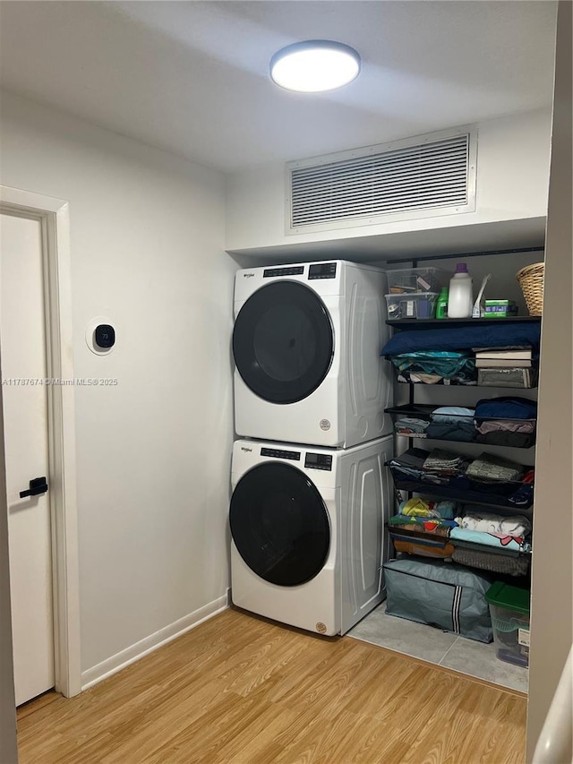 clothes washing area featuring stacked washing maching and dryer, visible vents, light wood finished floors, and laundry area