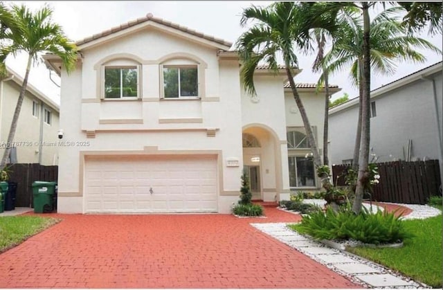 mediterranean / spanish-style home featuring stucco siding, an attached garage, fence, and decorative driveway