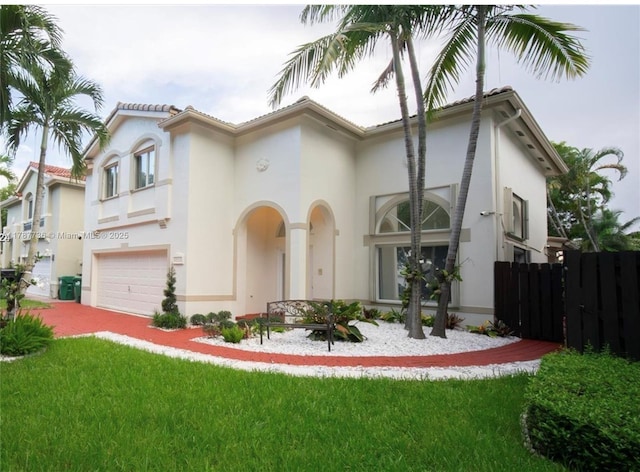 mediterranean / spanish-style house with an attached garage, a front lawn, stucco siding, and fence