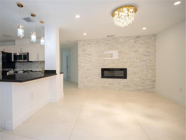 kitchen with white cabinets, dark countertops, stainless steel microwave, freestanding refrigerator, and a fireplace