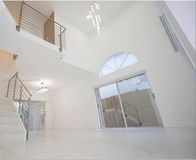 unfurnished room featuring a wealth of natural light, an inviting chandelier, a towering ceiling, and stairs