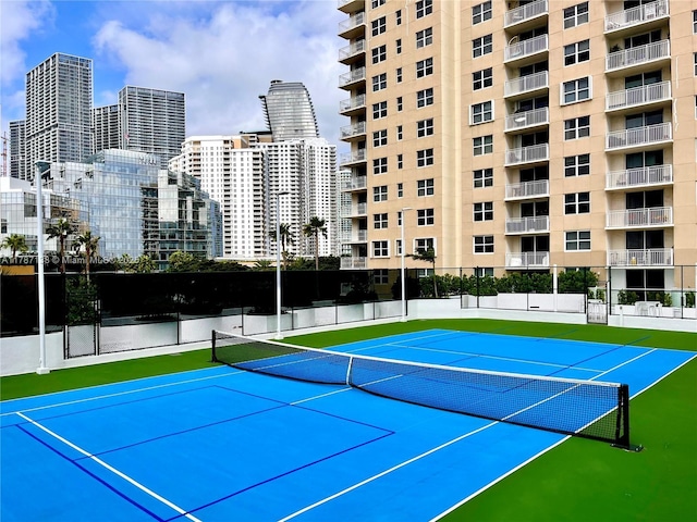 view of tennis court with fence, community basketball court, and a city view