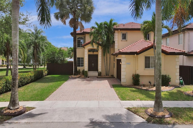 mediterranean / spanish house with fence, a tiled roof, a front yard, and stucco siding