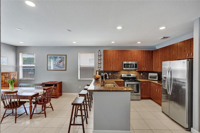 kitchen featuring a sink, brown cabinets, stainless steel appliances, backsplash, and a peninsula