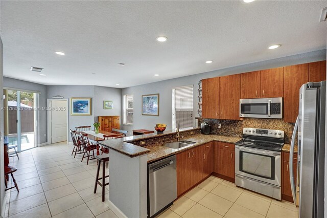 kitchen featuring a sink, brown cabinetry, stainless steel appliances, a peninsula, and recessed lighting