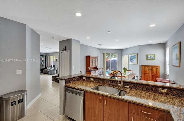 kitchen featuring brown cabinets, stainless steel dishwasher, light tile patterned floors, a sink, and dark stone counters