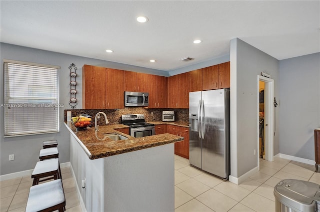 kitchen featuring stainless steel appliances, visible vents, a sink, a peninsula, and brown cabinetry