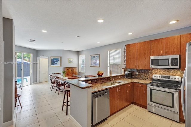 kitchen with brown cabinets, a peninsula, appliances with stainless steel finishes, and a sink