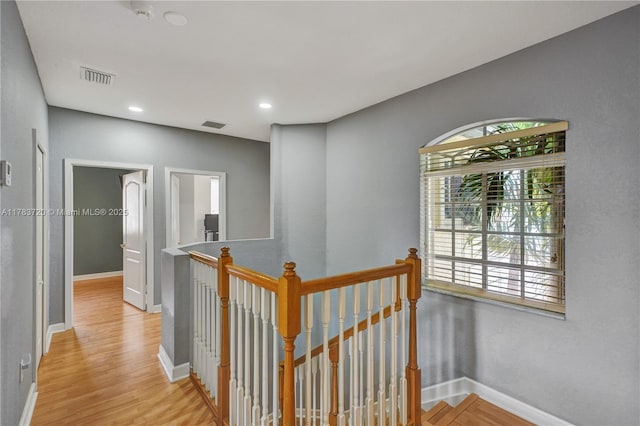 corridor with baseboards, light wood finished floors, an upstairs landing, and visible vents