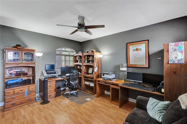 home office featuring a textured wall, light wood-style flooring, baseboards, and ceiling fan