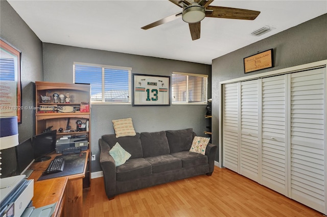 living room with a textured wall, visible vents, wood finished floors, baseboards, and ceiling fan