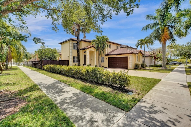 mediterranean / spanish-style home with stucco siding, driveway, a front yard, and fence