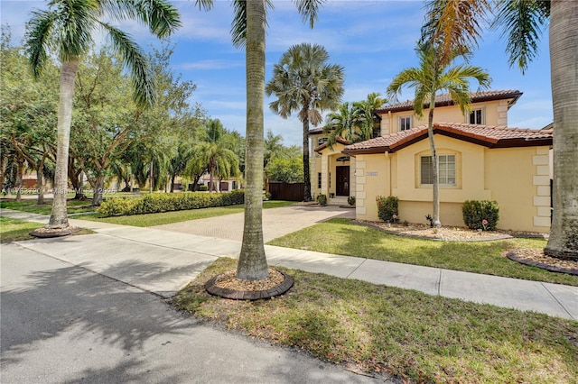 mediterranean / spanish-style home featuring fence, a tiled roof, a front lawn, concrete driveway, and stucco siding
