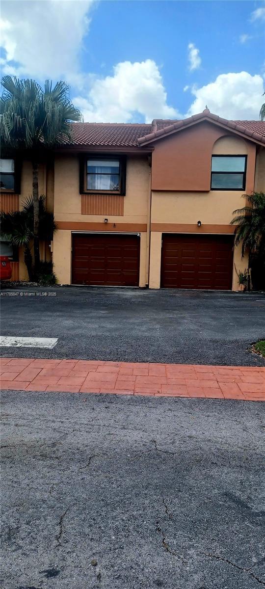 townhome / multi-family property with an attached garage, aphalt driveway, stucco siding, and a tile roof