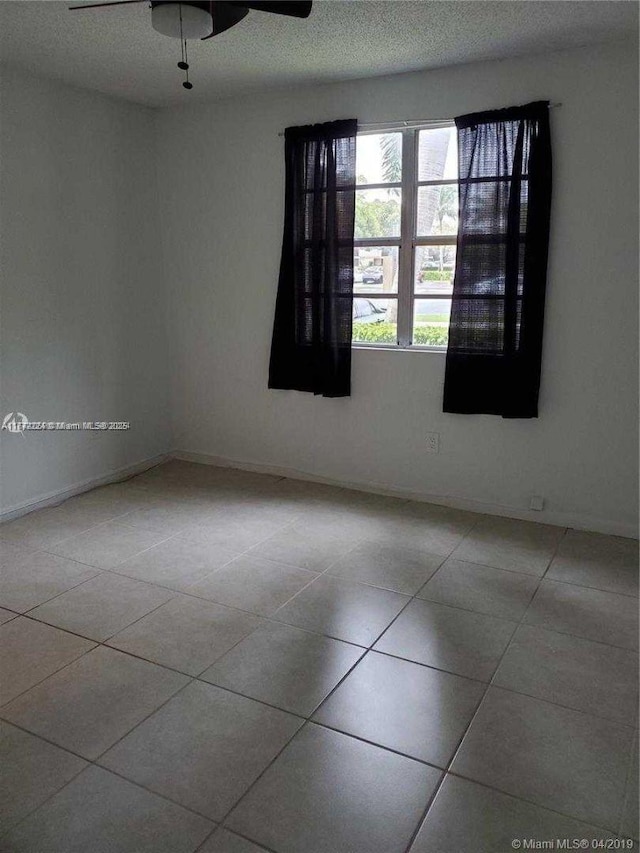 empty room featuring a ceiling fan, baseboards, and tile patterned flooring